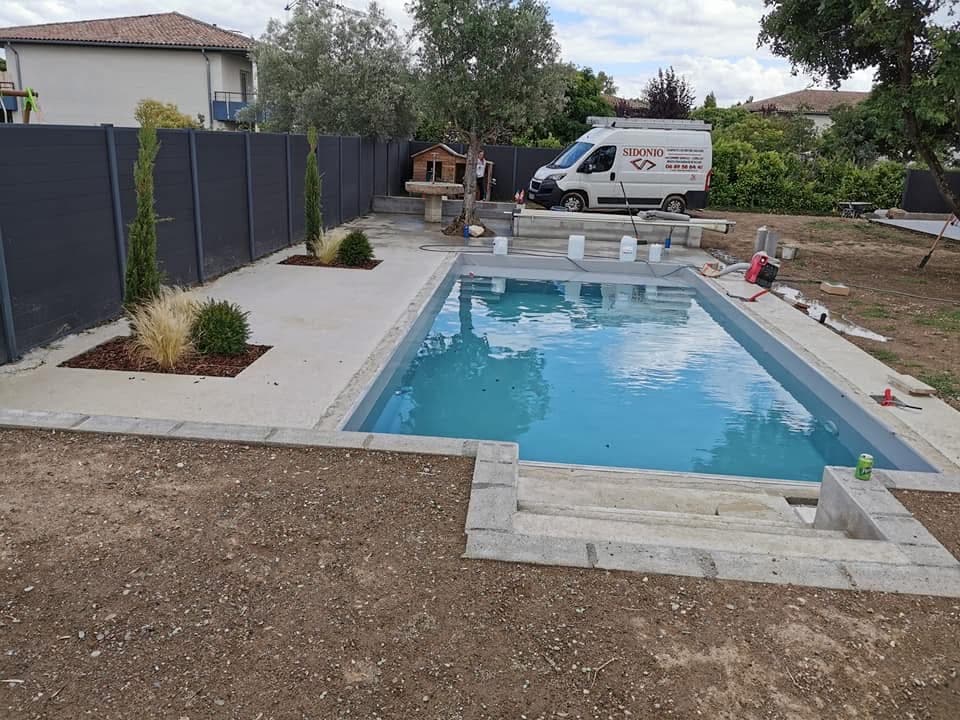 Chantier piscine en cours avec eau bleue, margelles en cours de finition et camionnette SIDONIO garée.