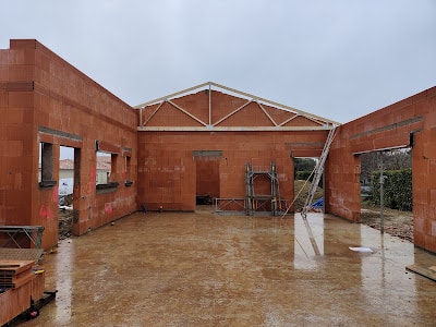 Construction maison : murs terre cuite et charpente neuve Construction d'une maison : murs en briques de terre cuite montés, charpente métallique du pignon installée, sol inondé par la pluie.