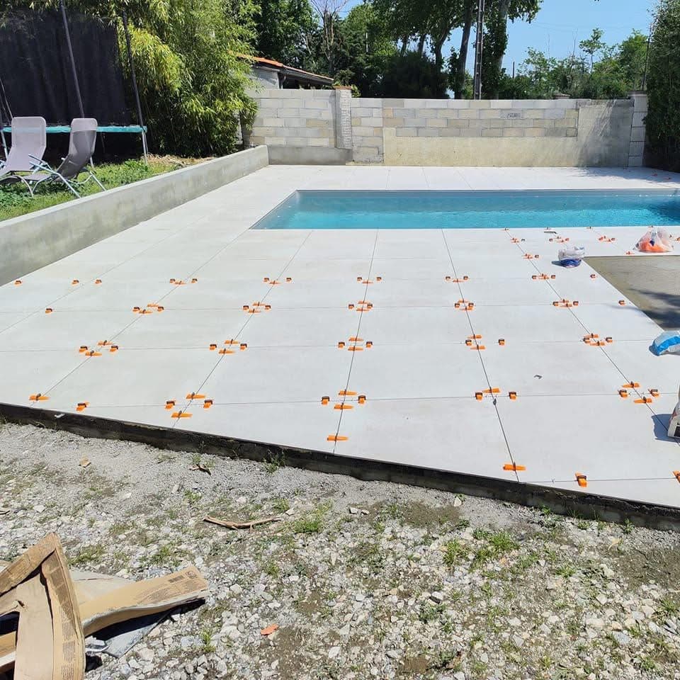 Pose de carrelage de terrasse autour d'une piscine avec des croisillons et cales de nivellement orange.