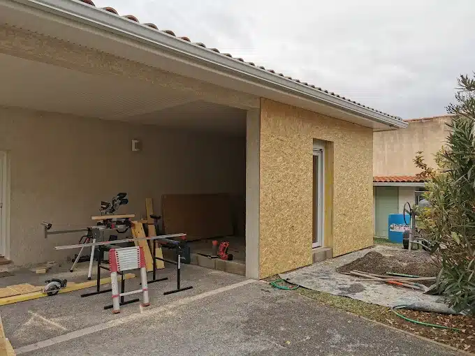 Rénovation Maison : Extension Moderne et Travaux en Cours Chantier de rénovation maison: extension avec mur en panneaux OSB et fenêtre. Outils de menuiserie, toiture à tuiles, gouttière blanche et matériaux.