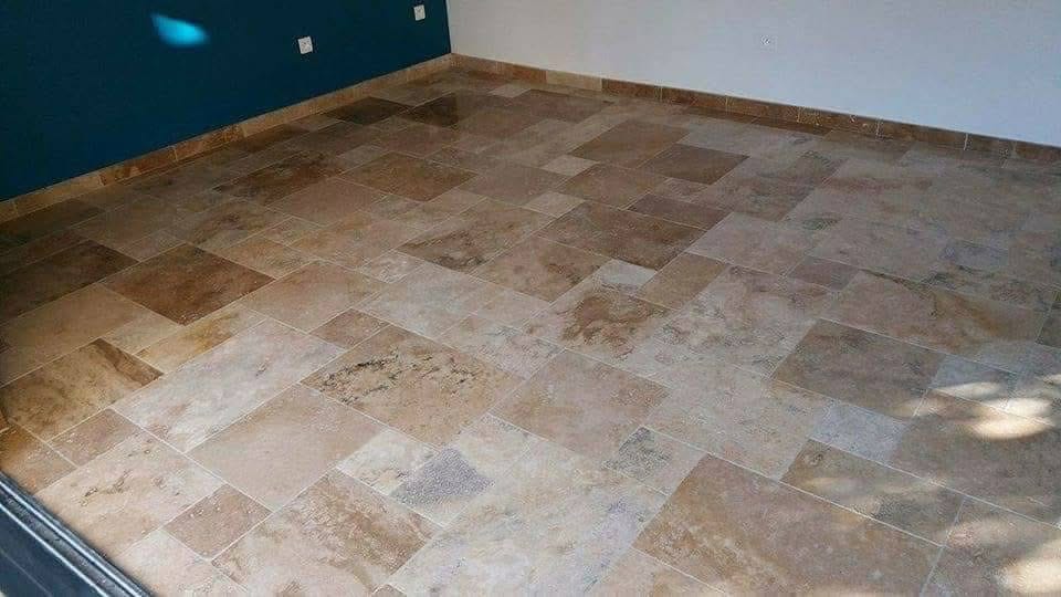 Sol carrelé en grandes dalles de travertin beige et marron, juxtaposition de tons clairs et foncés, sous un mur bleu sarcelle.