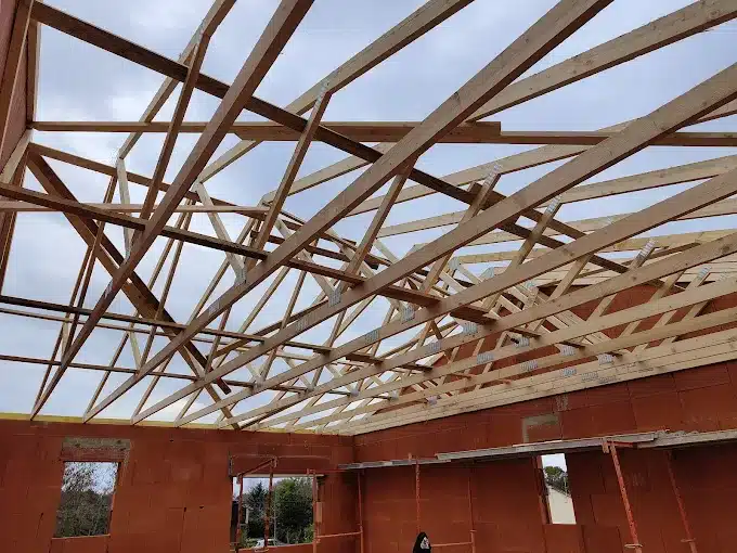 Charpente en bois sur murs de briques rouges d'une maison en construction sous un ciel gris.