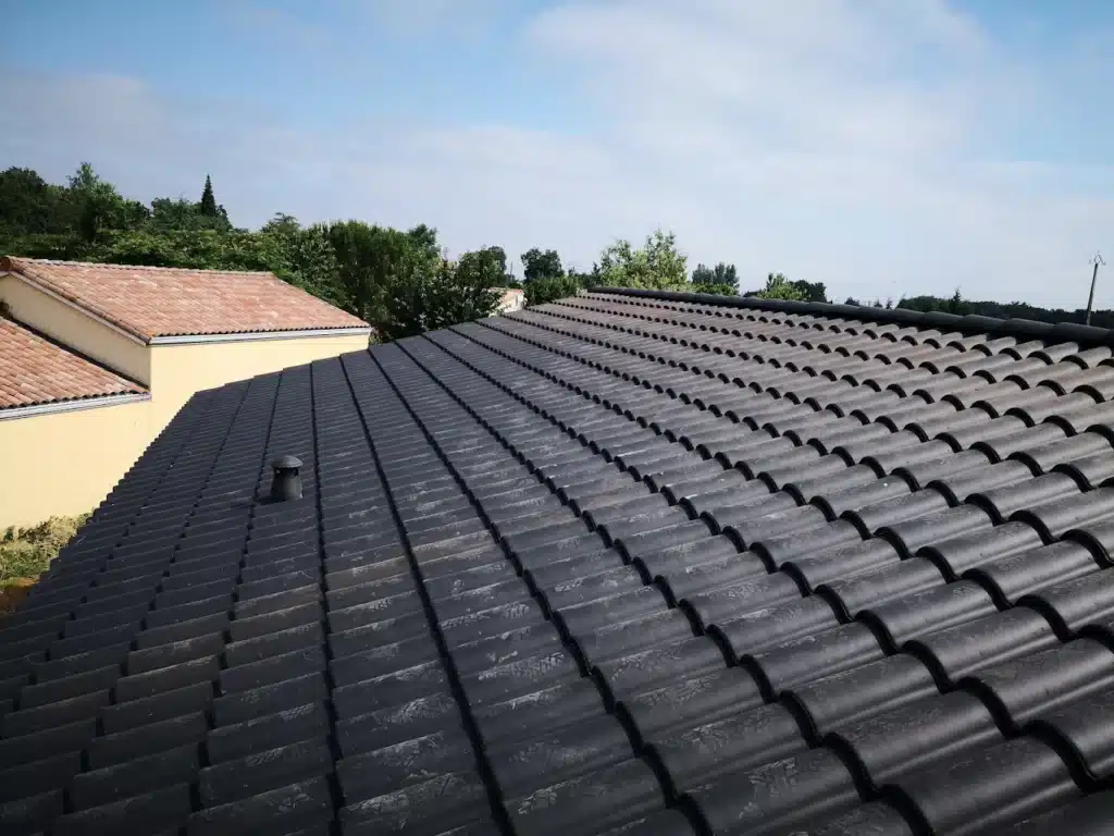 Toiture moderne en tuiles gris anthracite - Rénovation Toiture moderne en tuiles gris anthracite avec conduit d'aération sur fond de ciel bleu et arbres.