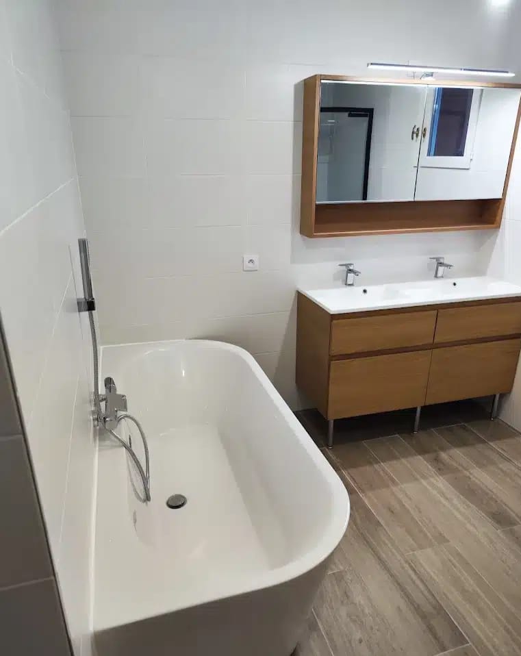 Salle de bain moderne avec baignoire et meuble double vasque Salle de bain moderne avec baignoire blanche, meuble double vasque en bois et carrelage au sol aspect parquet.
